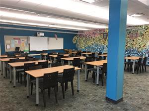 photo from the middle school library, of the classroom area. Depicts tables with chairs and a projection area in the back of the photo
