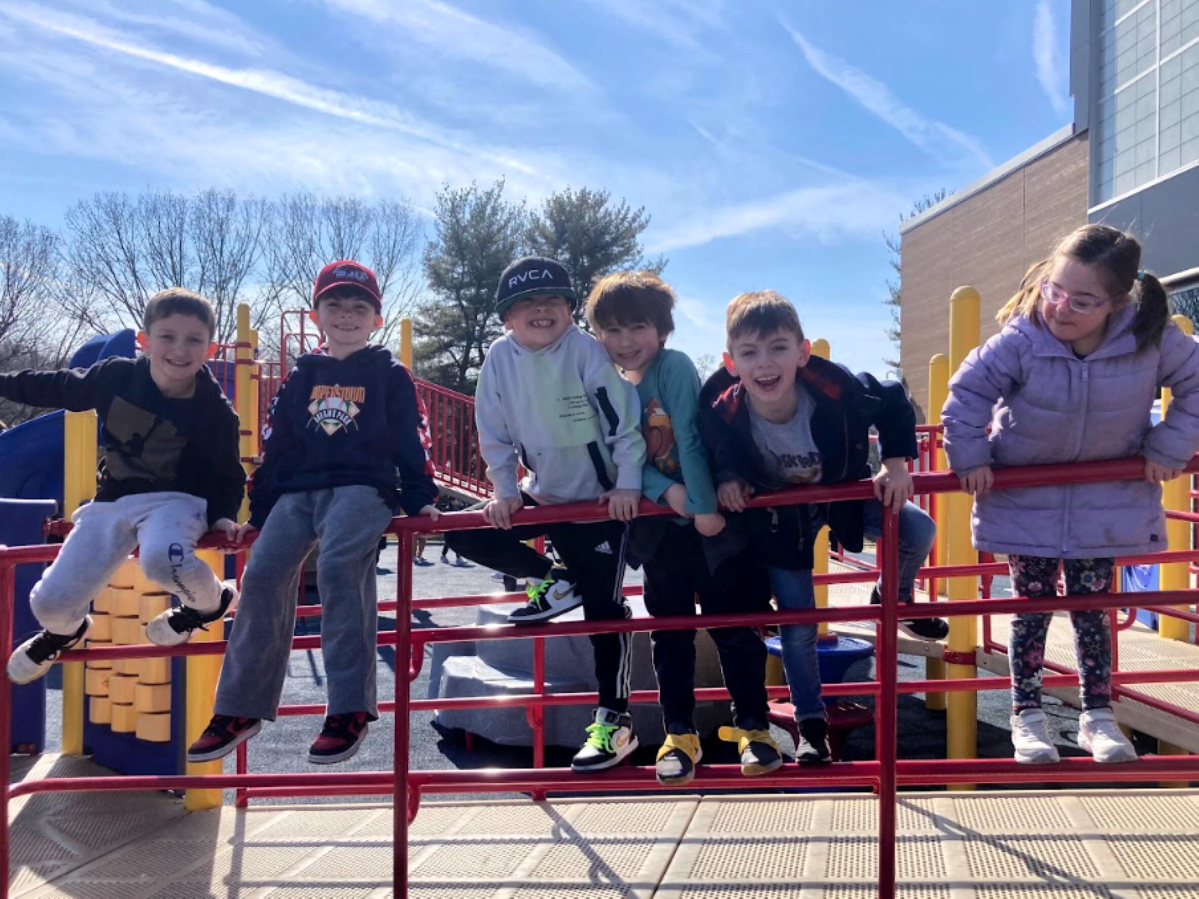 six students sitting and standing on a railing in the playground