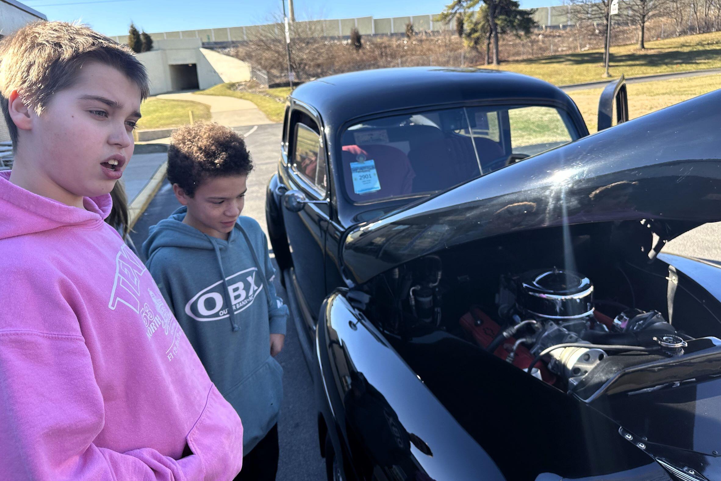 Two Students looking at an antique car. Car has hood open.